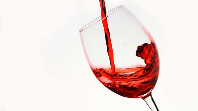 Elegant shot of red wine being poured into a tilting glass against a white background.