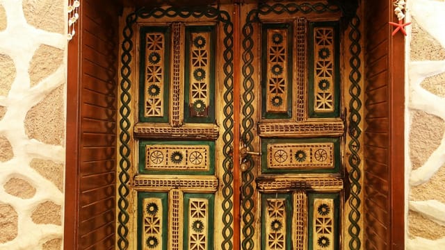 Intricately designed wooden door with geometric patterns and stone wall in Çiftlikzade Konağı.