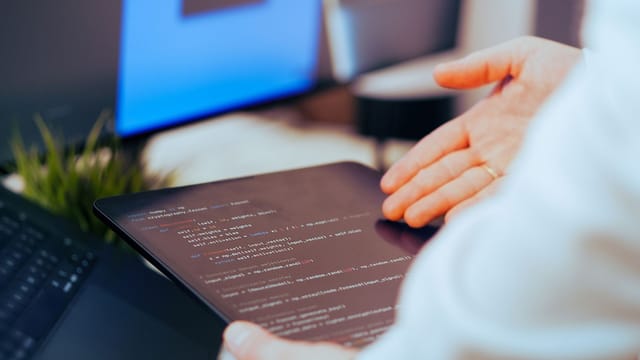 Software developer analyzing code on a tablet in a modern office workspace.
