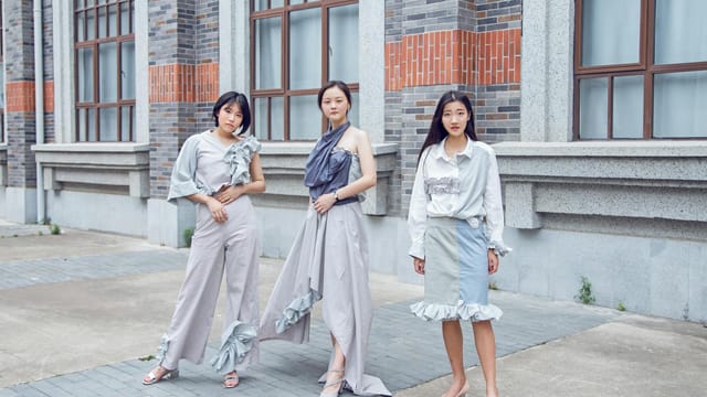 Three fashionable women pose confidently outdoors in stylish urban attire.