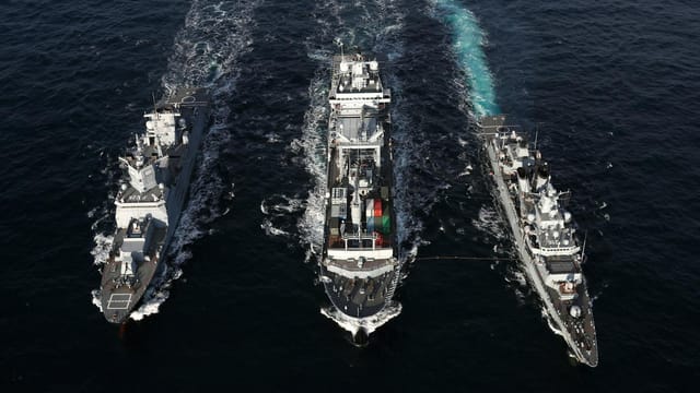 Naval ships sailing in formation on open sea, aerial view highlights naval coordination and strategy.