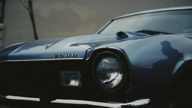 Detailed close-up of a vintage blue Ford car's headlight showcasing classic automotive design.
