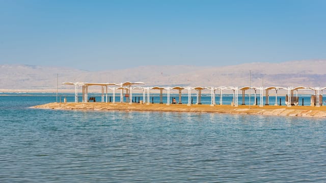 Peaceful beach with sunshades by the Dead Sea in Israel under a clear blue sky.