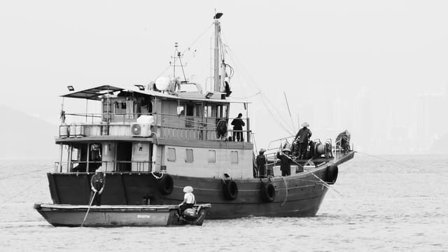 Black and white image of a traditional fishing boat in Hong Kong, featuring fishermen at work.