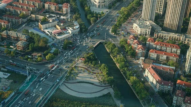 Aerial cityscape depicting bridges, roads, and waterways, showcasing urban architecture and traffic from above.