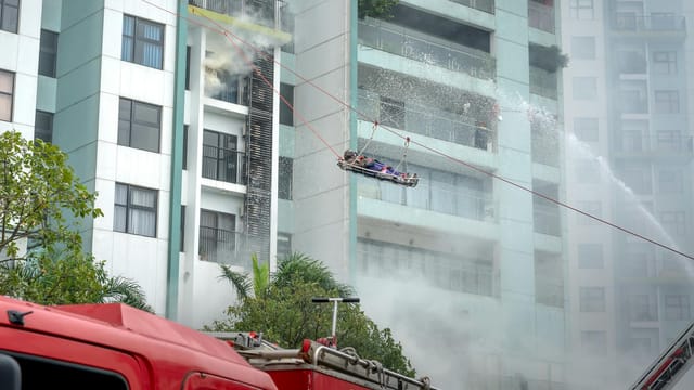 Firefighters using hoses and cranes to rescue residents from a burning high-rise urban apartment building.
