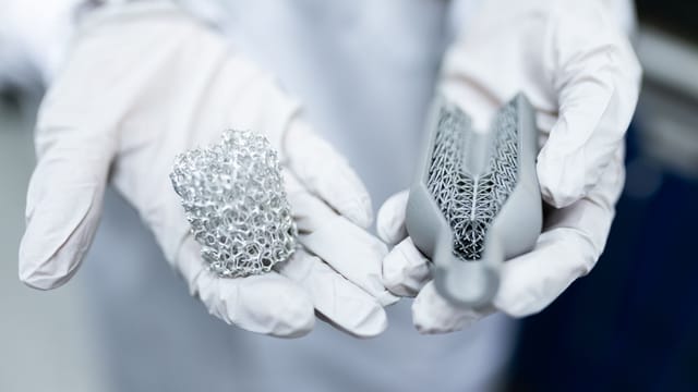 Laboratory setting showing gloved hands holding innovative 3D printed metal structures.
