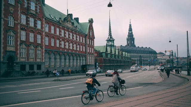 Cyclists riding along famous embankment in Copenhagen with historic Christiansborg palace and stock exchange building in Denmark on cloudy day