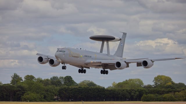 An AWACS surveillance aircraft landing on an outdoor runway with cloudy skies.
