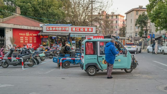 Vibrant city traffic with auto rickshaws and scooters on a lively street in Nantong, China.