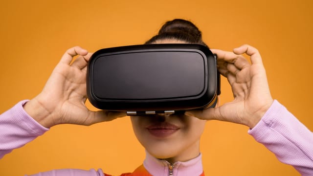 Close-up of a woman using a VR headset with an orange background.
