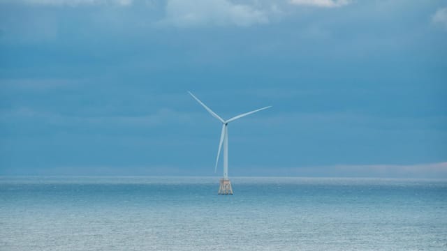 A solitary offshore wind turbine stands against a serene seascape in New Shoreham, RI, USA.