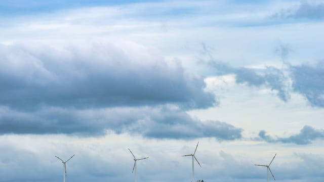 Scenic view of wind turbines on a hill with a cloudy sky, representing renewable energy.