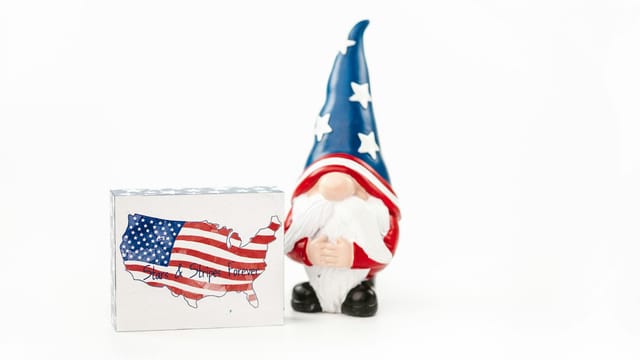 A whimsical gnome in USA colors next to a stars and stripes forever box.