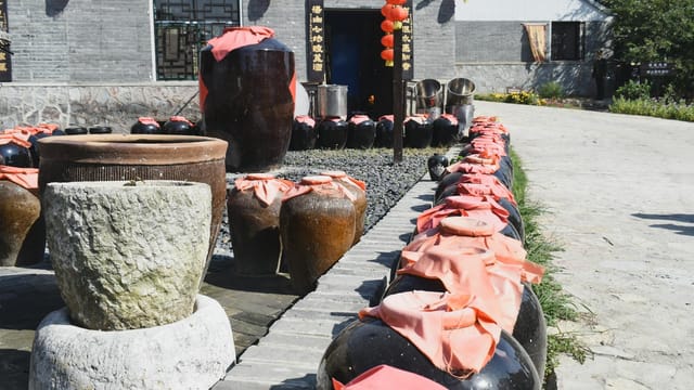 Rows of ceramic jars with red coverings in a sunny courtyard in Nanjing, China, symbolizing traditional winemaking.