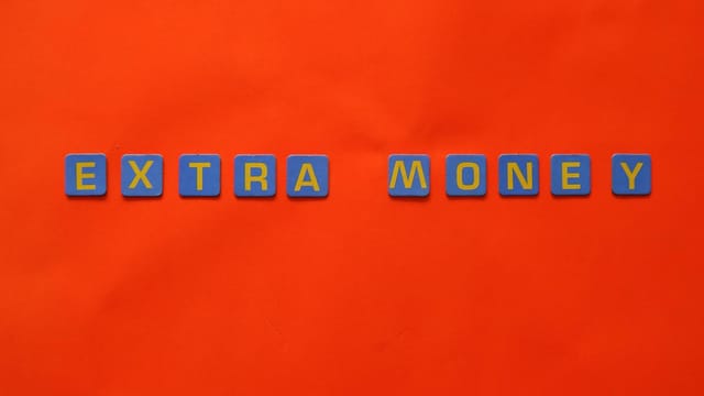 Bright orange background with 'EXTRA MONEY' spelled in blue and yellow tiles, illustrating financial concepts.
