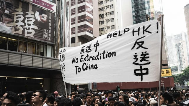 Protesters in Hong Kong holding banners against extradition to China, urban backdrop.