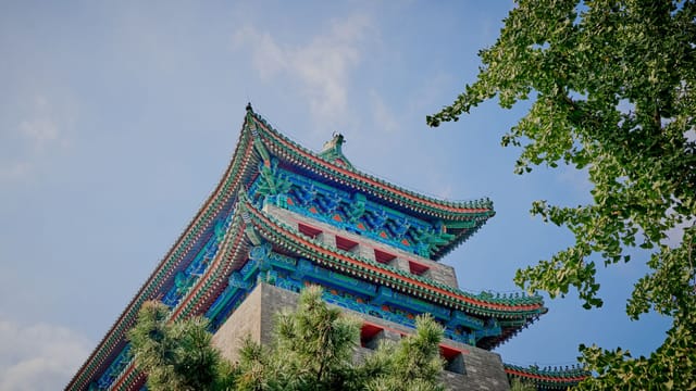 Ornate traditional Chinese temple roof with vibrant colors and trees beneath a clear blue sky.
