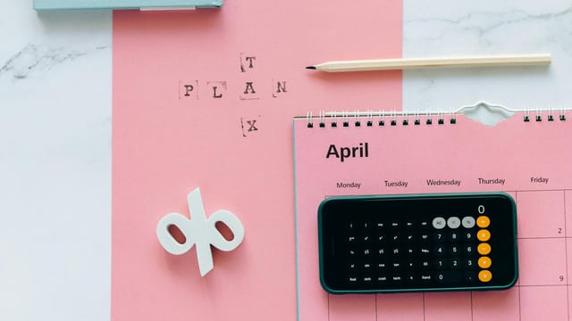 Flat lay of April calendar with calculator, pencil, and pink background for financial planning.