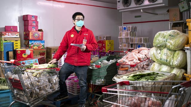Asian man wearing red jacket and mask working in a store with shopping carts in Wuhan, China.