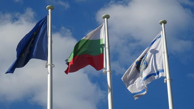 Three flags, including Bulgaria and EU, waving under a blue sky.