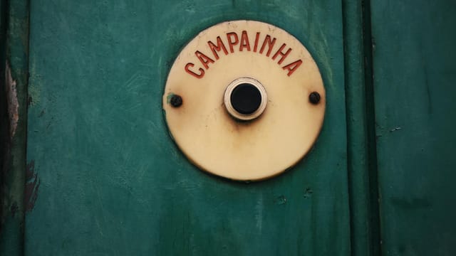 Close-up of a vintage doorbell with 'Campainha' text on a rustic green background.