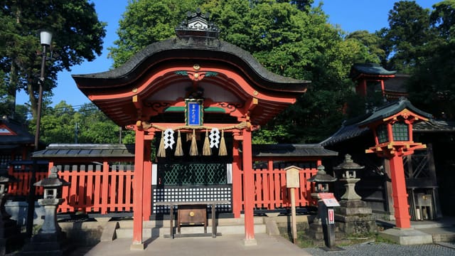 A stunning view of a traditional Japanese shrine with vibrant red accents surrounded by lush greenery under a blue sky.