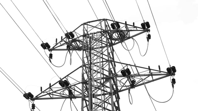 Black and white photo of high voltage power lines and electrical tower against a clear sky.