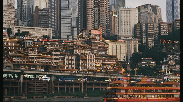 Colorful Chongqing buildings and riverboat illuminate the night, showcasing urban vibrancy.