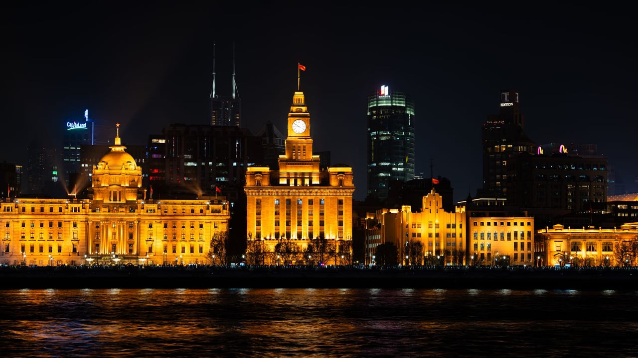 Dramatic night view of Shanghai Bund with illuminated buildings reflecting on water.