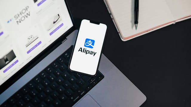 Smartphone displaying Alipay app on open laptop with online shopping site.