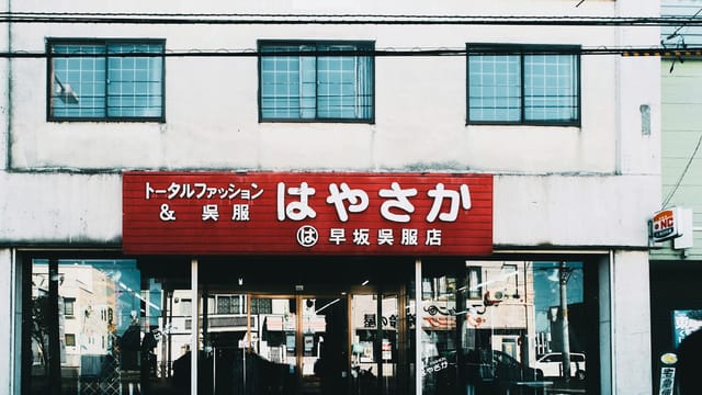 Street view of a Japanese clothing shop with a prominent red sign and glass windows.