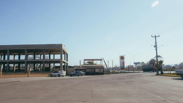 An urban gas station with empty parking spaces and visible signage under a clear sky.
