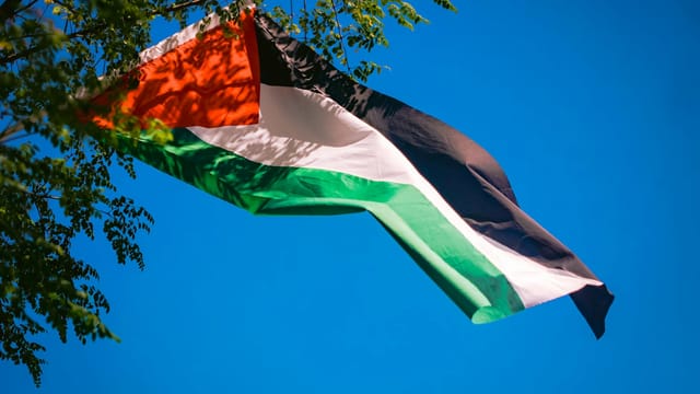 Vibrant Palestinian flag waving against a clear blue sky, representing freedom and patriotism.