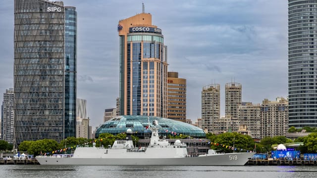 Contemporary skyline of Shanghai with a naval ship anchored, capturing urban architecture and maritime activity.