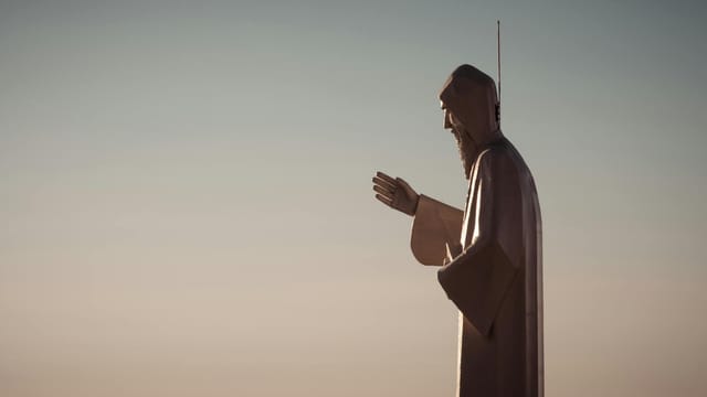 Side view of the Mar Charbel statue in Faraiya, Lebanon, beautifully silhouetted against a sunset sky.