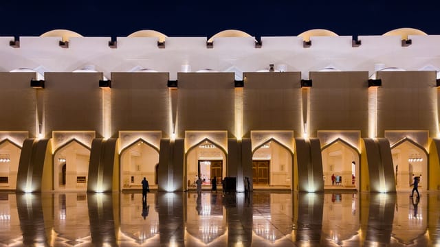 A beautifully illuminated mosque facade reflecting on a shiny surface in Doha, Qatar at night.