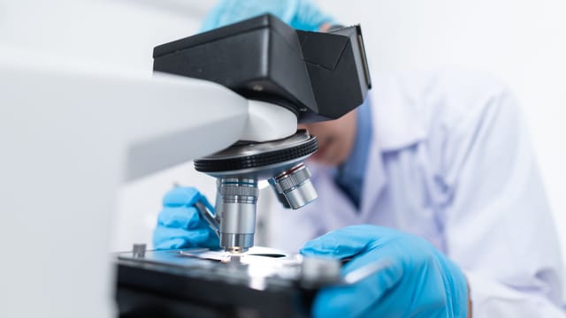 Close-up of a scientist examining samples under a microscope in a lab setting.
