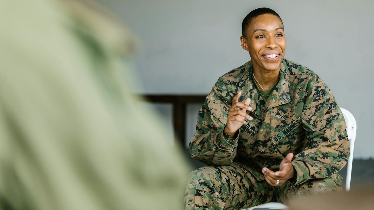 A joyful soldier in uniform participates in a supportive group session indoors.