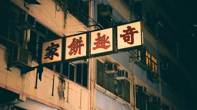 Street view of a neon-lit sign on a building facade at night in a bustling urban area.