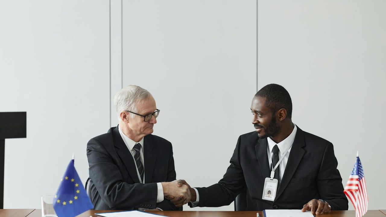 Corporate handshake between diverse businessmen representing EU and US flags, symbolizing partnership and collaboration.