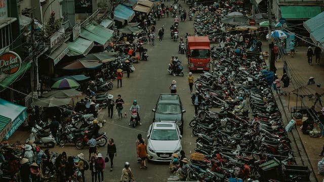 A bustling outdoor market with crowded streets filled with people and motorcycles.