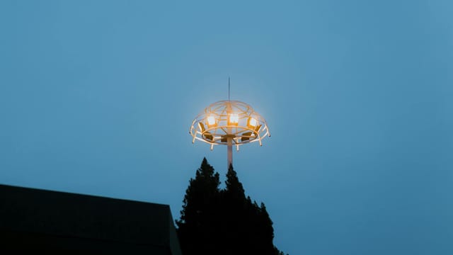 A glowing UFO-like structure on a pole against a clear evening sky, creating a mysterious urban scene.