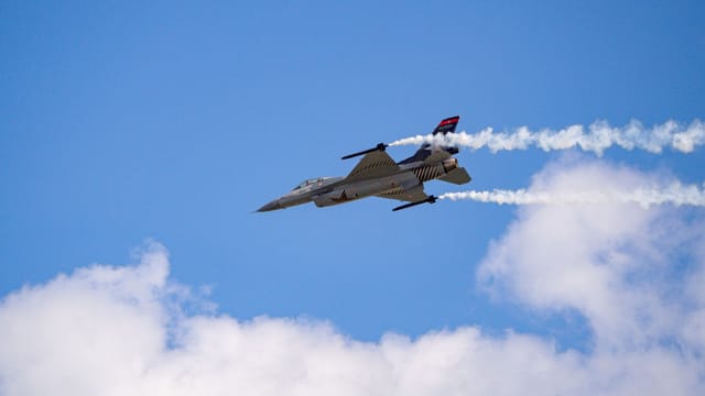 Turkish Air Force fighter jet flying in clear blue sky with smoke trails.