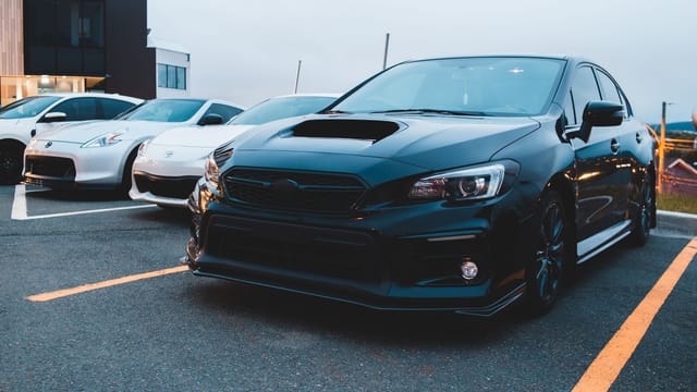 Powerful black automobile with massive hood standing near modern racing white cars on asphalt parking lots