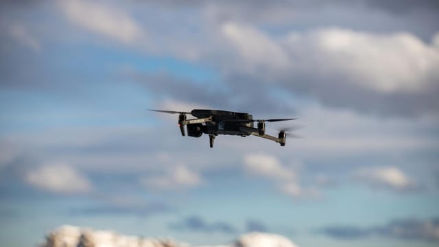 Aerial view of a drone flying over snow-covered mountains with dramatic clouds.