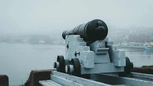 A historic cannon aimed at the misty seaside from a fortress, evoking a sense of defense and history.