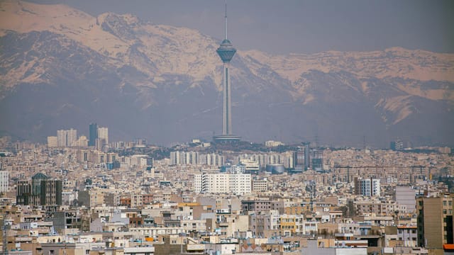 Aerial view of Tehran featuring Milad Tower against the Alborz Mountains.