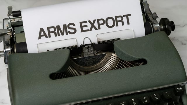 Close-up of a vintage typewriter with the text 'Arms Export' on paper, focusing on journalism and government topics.