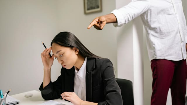 An office scenario depicting a young woman experiencing bullying from a coworker.